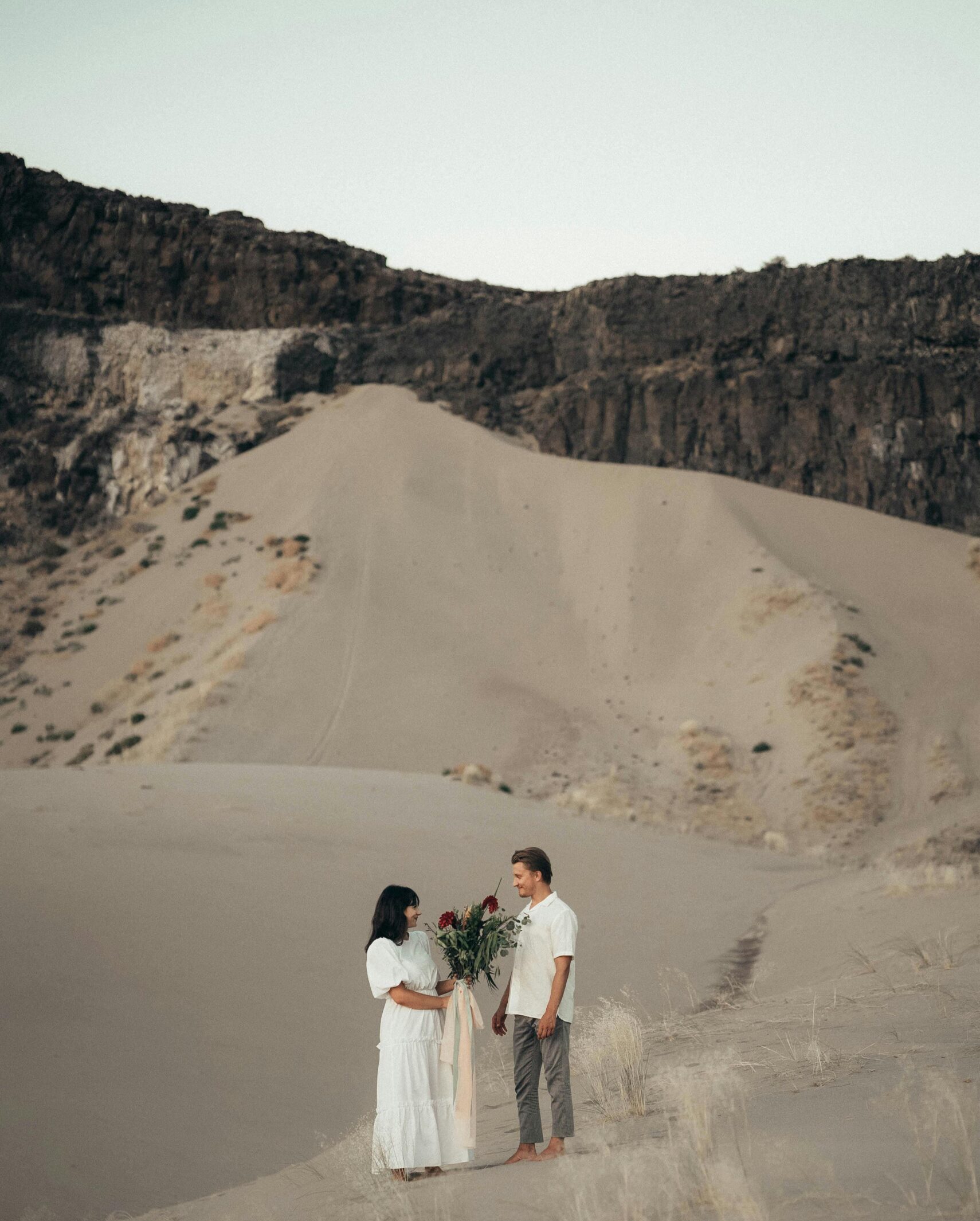 Young man and woman with flowers standing on sandy hill and enjoying holidays together in desert