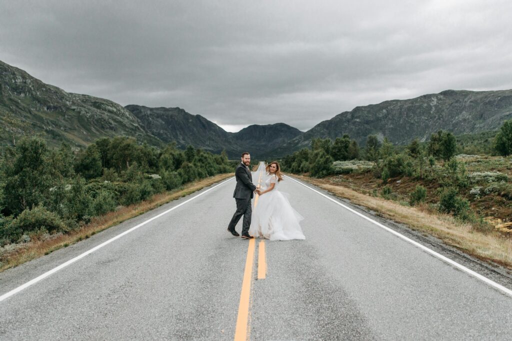 Bride and groom on a scenic mountain road, embracing nature with love and joy.